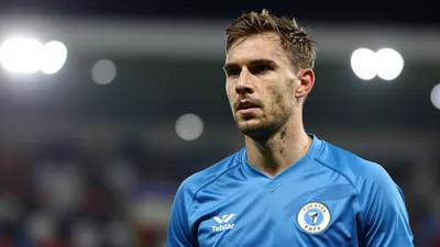 A mid-30s Telstar goalkeeper in a solid blue jersey, head-and-shoulders, focused expression, background blurred stadium...