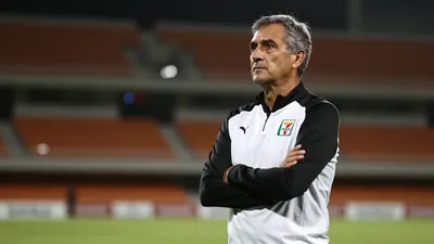 A 50-year-old male coach in a black and white plain unmarked training top, with a rugged complexion and a few wisps of...