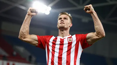 A tight action shot of a tall, muscular Icelander in a red and white striped shirt, mid-celebration after scoring, arms...